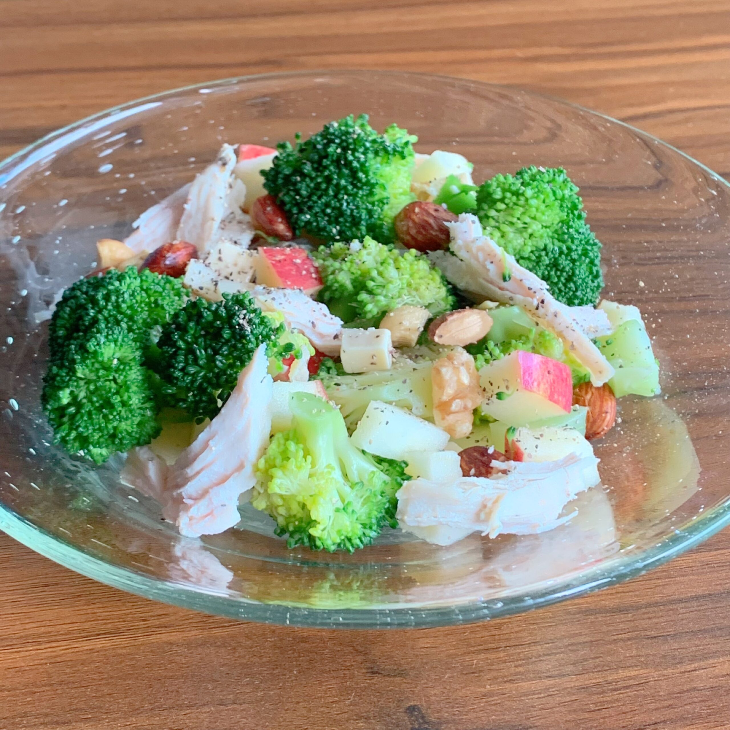 A salad made with steamed chicken, broccoli, apples, and nuts. 