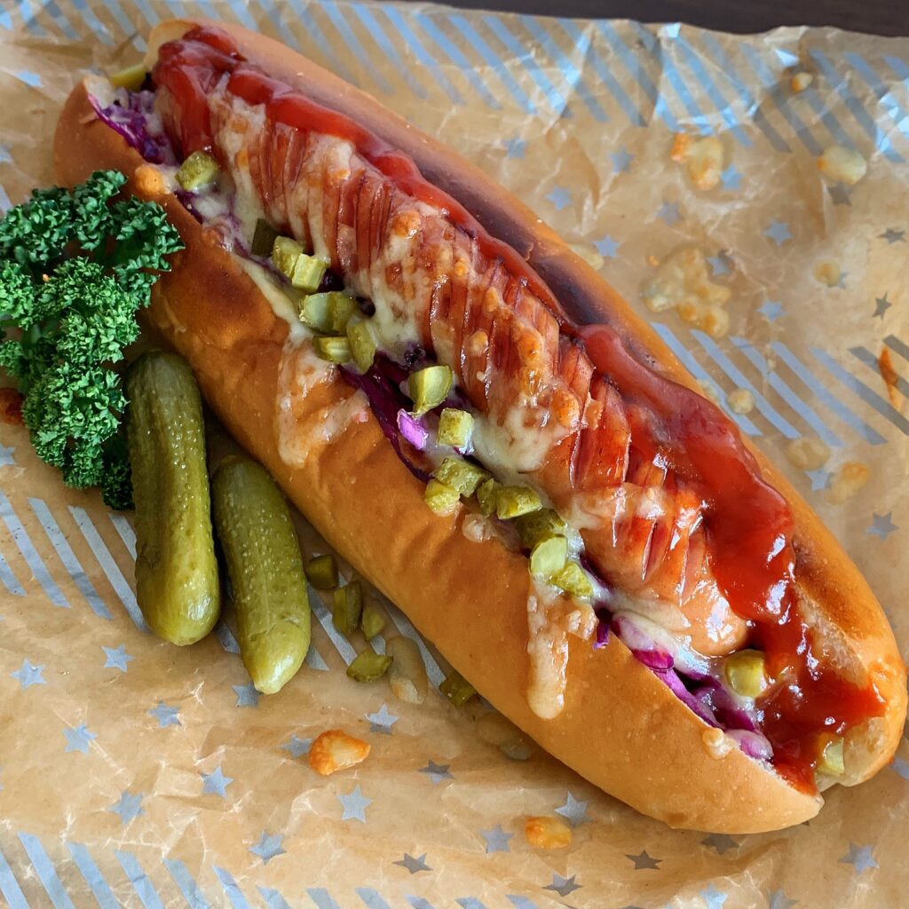 Wiener sausage, salsa sauce, and marinated purple cabbage are sandwiched between hot dog bun. 