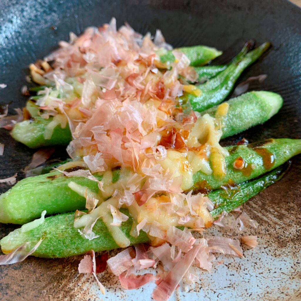 Okra is grilled and topped with cheese and bonito flakes. Cheese, bonito flakes, and soy sauce are all fermented foods, so they go together perfectly.